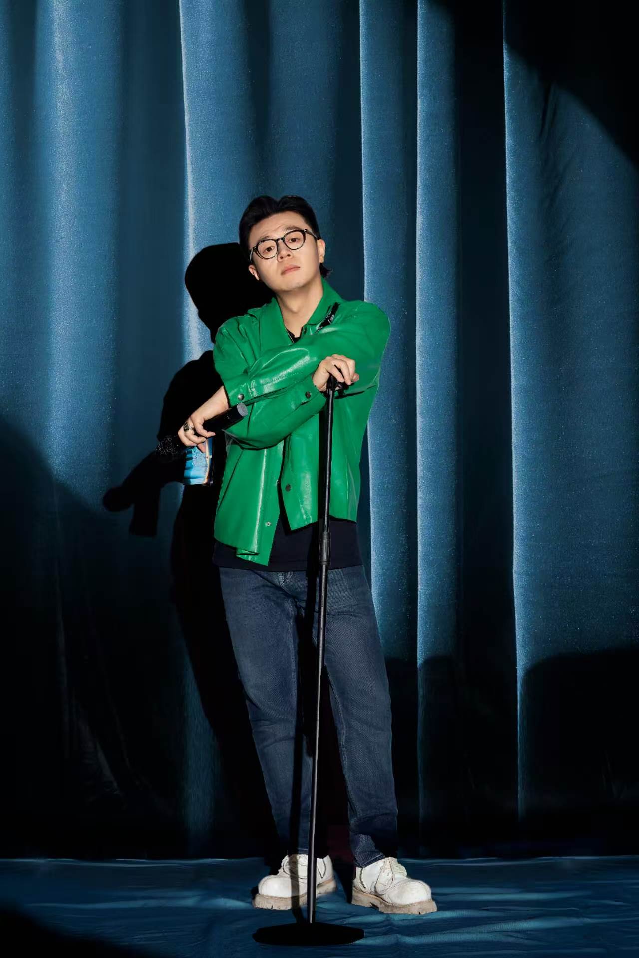意辰身穿绿色外套,手持麦克风站在深蓝幕布前